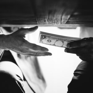 Two people exchanging a stack of money secretly under a table.