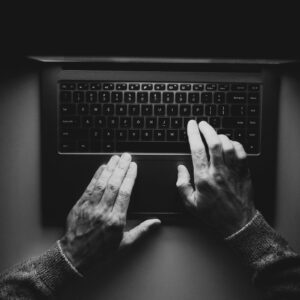 Overhead black and white photo of a person typing on a laptop in a darkened setting.